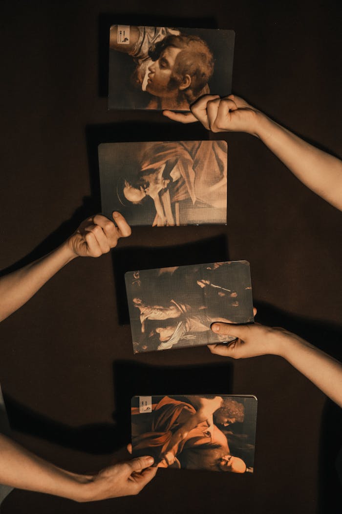 Four hands holding art prints against a dark backdrop, featuring classical paintings.