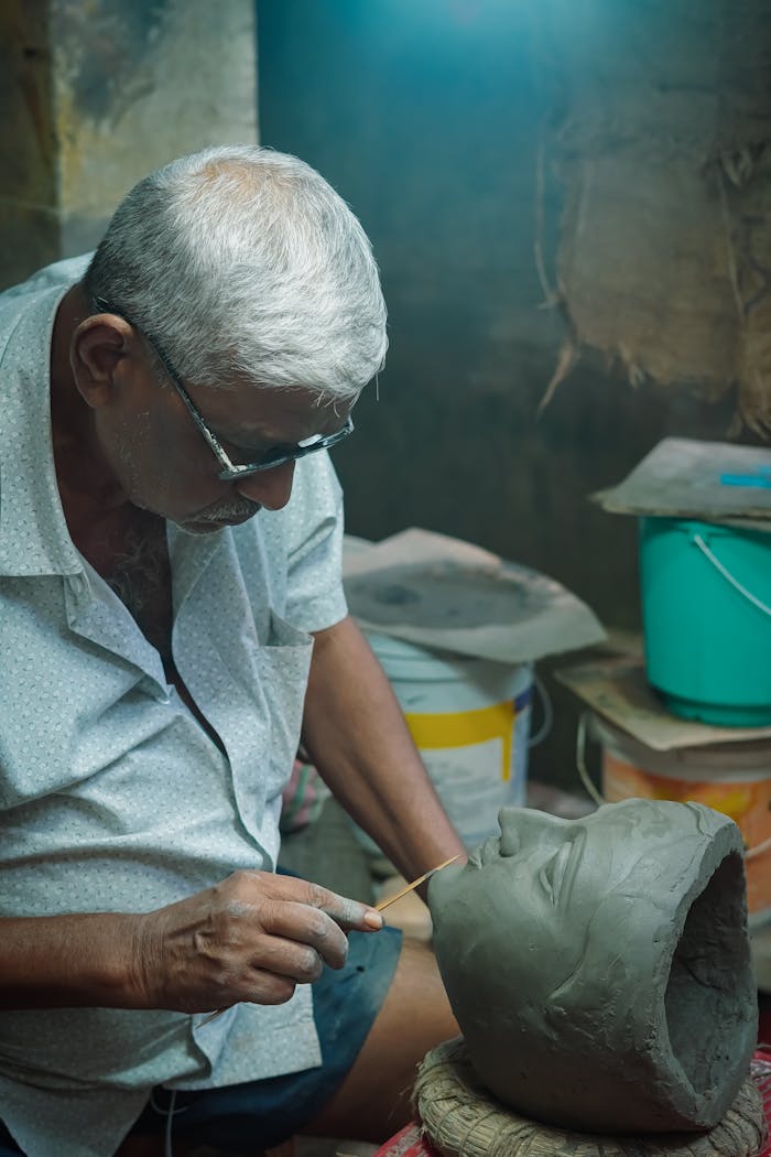 services-01 An elderly sculptor skillfully crafts a clay statue in his Kolkata workshop, showcasing artistic craftsmanship.