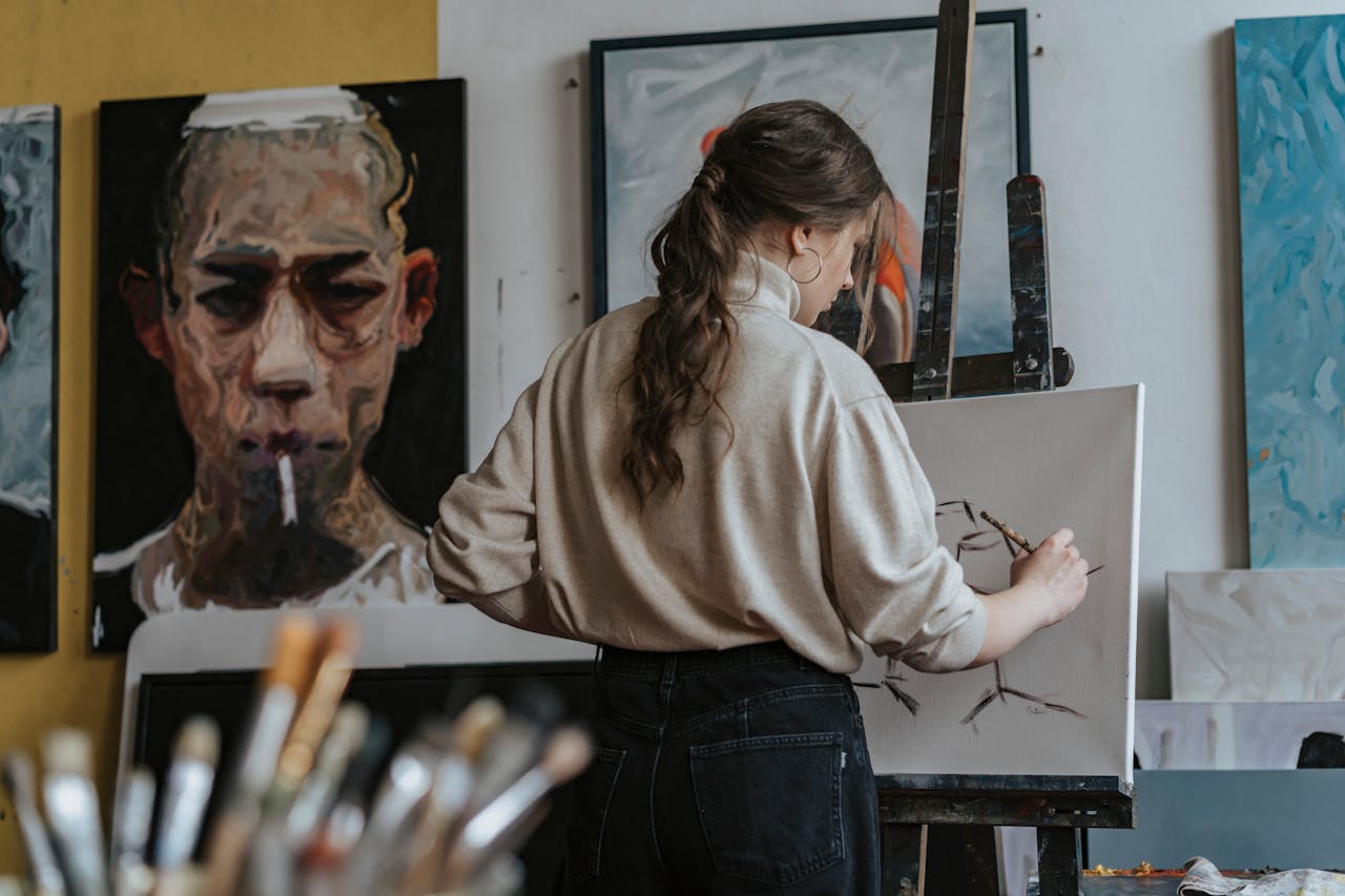 services-03 Female artist working on a canvas in a studio with paintings in the background.