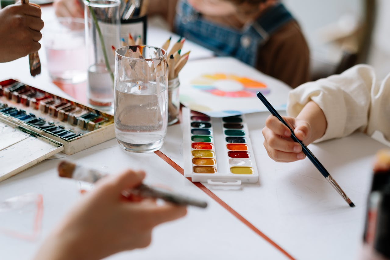 who-we-are Children's hands holding paintbrushes while painting with watercolors during a creative art session.